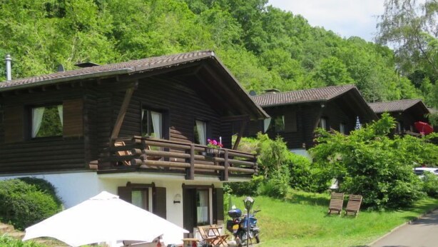 Een houten hut met een balkon, omgeven door weelderige begroeiing en een heldere lucht.