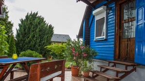 Une terrasse avec des bancs en bois et une table, entourée de plantes en pot et d’une maison bleue.