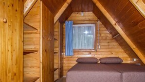 Une pièce en bois avec un plafond en pente, un lit avec des oreillers, une fenêtre avec un rideau et des murs en bois.