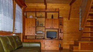 L’intérieur d’un chalet accueillant, avec un canapé en cuir vert, des étagères en bois ornées de divers objets, un téléviseur et un escalier.