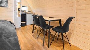 Een gezellige kamer met houten plafond, een kleine kitchenette, een eettafel met vier stoelen en een bed met grijze plaid.