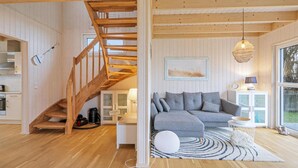 Un'ampia zona giorno con una scala in legno, un divano modulare grigio, un poggiapiedi bianco rotondo e un lampadario a sospensione.
