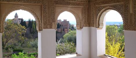 A room with three arched windows overlooking a historic building and a garden.