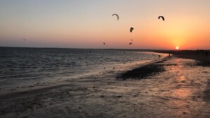 Une plage au coucher du soleil, avec des cerfs-volants qui volent au-dessus de l’eau.