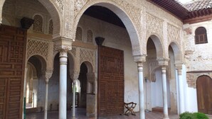 Une cour intérieure agrémentée d’arches et de colonnes décoratives, d’une porte en bois et d’un banc.