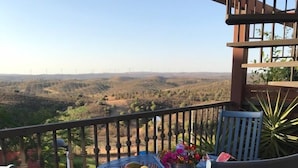 Un balcon avec une table ronde et des chaises, un panier de fruits et un vase de fleurs.