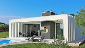 Ein modernes Haus mit Pool, Sitzgelegenheiten im Freien und blauem Himmel.