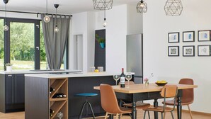Eine moderne Küche mit Kochinsel, Pendelleuchten und einem Essbereich mit Stühlen und Tisch.