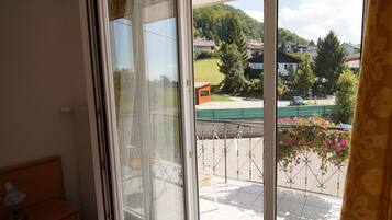 Une pièce dotée d’une porte-fenêtre coulissante donnant sur un balcon avec vue sur des maisons et de la verdure.