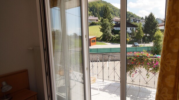 Ein Zimmer mit einer Schiebeglastür, die auf einen Balkon mit Blick auf Häuser und Grünflächen führt.