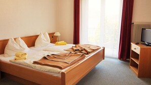 Ein Hotelzimmer mit Bett, Fernseher, Schreibtisch und einem Fenster mit Vorhängen.