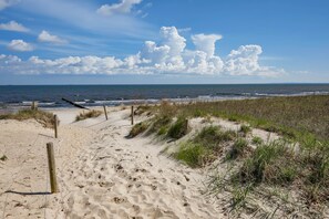 Un sentiero sabbioso che conduce all'oceano, con una recinzione di legno e dune erbose.