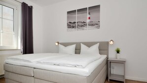 A bedroom with a bed, a nightstand, a potted plant, and a window with curtains. - Cozy vacation apartment in Koserow with terrace - only 350 m to the beach (Koserow)
