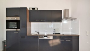 A modern kitchen with dark cabinetry, a built-in oven, a dishwasher, and a stainless steel range hood. - Cozy vacation apartment in Koserow with terrace - only 350 m to the beach (Koserow)