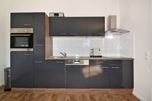 Una cucina moderna con mobili scuri, forno integrato, lavastoviglie e cappa aspirante in acciaio inossidabile.