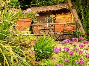 A rustic wooden hut with a thatched roof, surrounded by lush greenery and flowering plants. - Dreamland—plenty of space for up to 5 guests (Überlingen, Baden-Württemberg, Germany)
