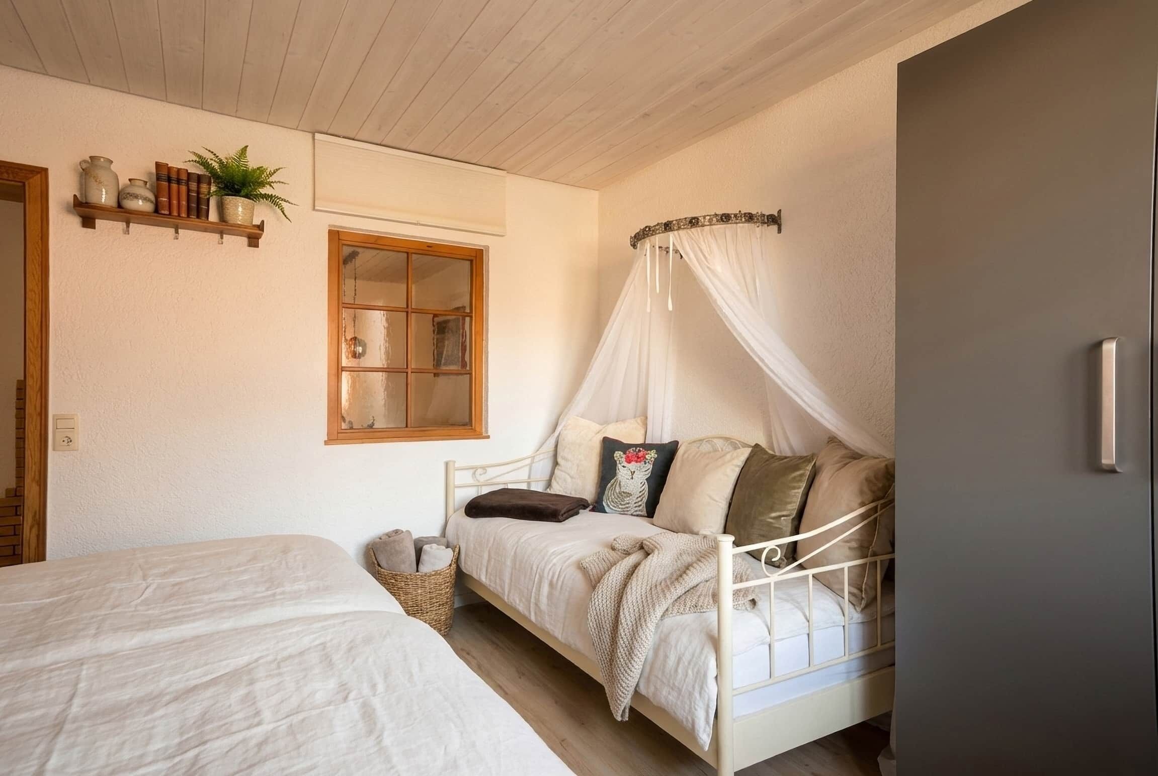 A bedroom with a bed, a bedside table, a window, a shelf with books and a plant, and a canopy bed.