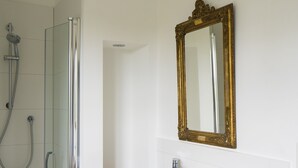 Een badkamer met een glazen douchecabine, een houten wastafelmeubel met een wastafel en een spiegel met een sierlijk omlijsting.
