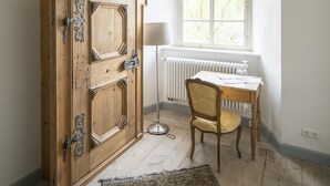 Een kamer met een houten garderobe, een bureau met stoel, een radiator en een raam met uitzicht op bomen.