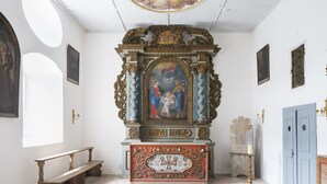 Een kapel met een versierd altaar, een houten bank en een blauwe deur.