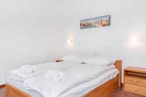 A neatly made bed with white linens and towels, a wooden nightstand with drawers, and a painting of a beach scene on the wall. - Cozy Apartment | Close to the Beach | Balcony (Miedzyzdroje)