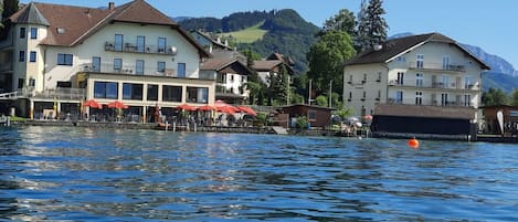 A lakeside hotel with multiple balconies, outdoor seating, and a view of the lake and mountains.