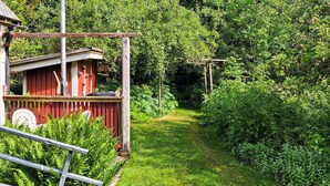 A red wooden structure with a balcony, surrounded by lush greenery and a clear path. - Pet friendly home in Hörby with WiFi (Hörby)
