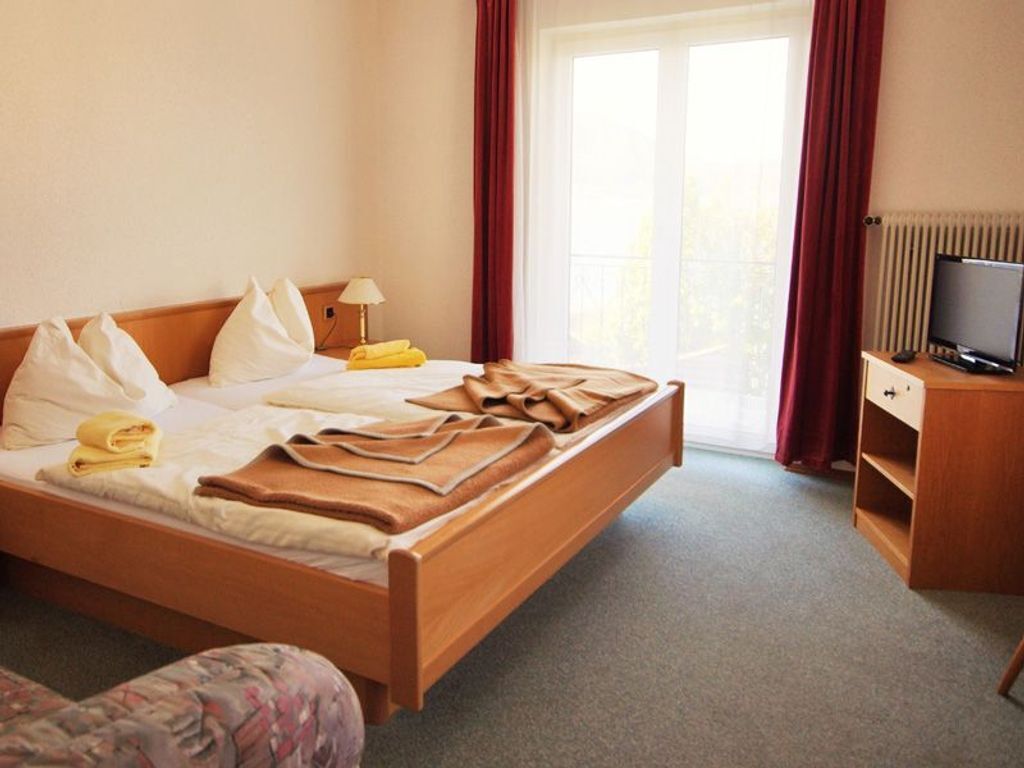 Ein Hotelzimmer mit Bett, Fernseher, Schreibtisch und einem fenster mit Vorhängen.