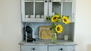 A light grey cabinet with glass doors and floral engravings, a wooden cutting board, a coffee maker, and a vase with sunflowers. - Fewo star view in a very quiet location in Beelitz (Beelitz)