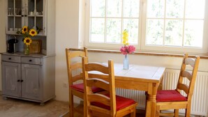 A dining area with a wooden table and chairs, a cabinet with glass doors, and a window with a view of greenery. - Fewo star view in a very quiet location in Beelitz (Beelitz)