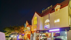 A hotel with a two-story structure, a covered outdoor area with lights, and multiple parked cars.