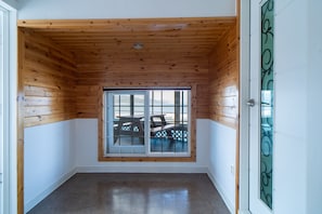A room with wooden ceiling and white walls, a sliding glass door leading to an outdoor area with a table and chairs.