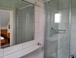 Moderni kylpyhuone, jossa on lasinen suihkuseinä, valkoinen kylpyamme ja suuri peili.