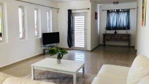 A spacious living room with a flat-screen TV, a coffee table with a plant, and a sofa. - Villa Brakkeput 308 (Jan Thiel)