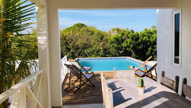 A pool area with a wooden deck, two lounge chairs, and a table with a cactus. - Villa Brakkeput 308 (Jan Thiel)