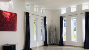 A spacious room with large windows, a tiled floor, and a red abstract painting on the wall. - Villa Brakkeput 308 (Jan Thiel)