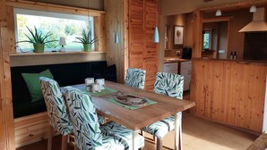 Una habitación acogedora de estilo cabaña con una mesa de comedor de madera, sillas tapizadas en verde, un banco empotrado y una zona de cocina con barra.