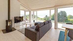 A modern living room with a large sofa, a TV, and a fireplace. There is a balcony with a view of the outdoors. - 3 bedroom nice home in Kalundborg (Kalundborg)