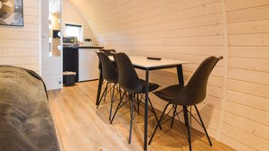 A compact room with a dining table and four chairs, a kitchenette in the background, and a wooden sloped ceiling. - 2 bedroom nice apartment in Nørre Nebel (Nørre Nebel)