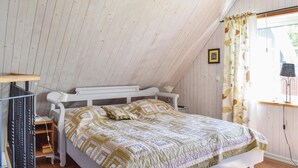 Une chambre avec un plafond en pente, un lit recouvert d’une courtepointe à motifs, une table de chevet et une fenêtre avec des rideaux.