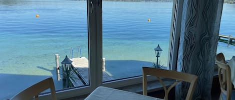 Una habitación con un ventanal grande que da a una superficie de agua tranquila, una mesa de madera y sillas.