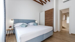 A modern bedroom with a large bed, a wooden headboard, a small bedside table with a lamp, and a view of the bathroom through an open door. - Gorgeous home in Sibenik (Sibenik)