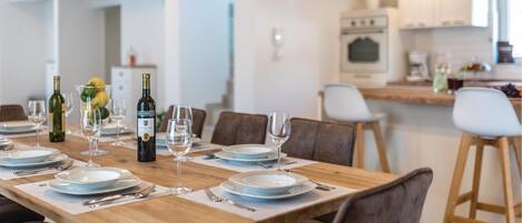Un comedor con una mesa de madera dispuesta para seis personas, rodeada de sillas. Hay una botella de vino y copas sobre la mesa.