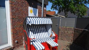 Ein roter und weiß gestreifter Gartenstuhl mit passendem Sonnenschirm vor einem Ziegelgebäude mit Fenster und Tür.