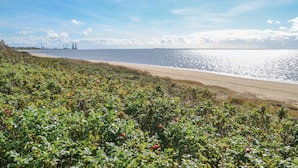 En strand med fri utsikt över havet och avlägsna industriområden.