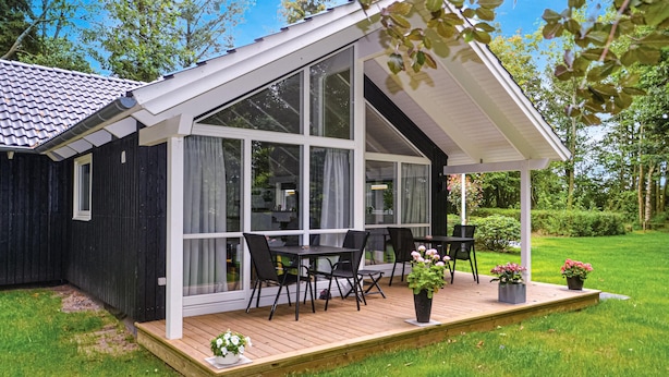 Ett modernt hus med en täckt uteplats, stora fönster och ett trädäck.