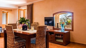 A dining area with a wooden table and wicker chairs, a flat-screen TV, and a window with a view of the outdoors. - Finca Capote, private pool, WIFI, A/C, 3 bedrooms, 2.5 bathrooms, 6 persons (Buger)