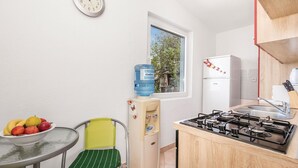 Cocina compacta con estufa a gas, dispensador de agua, refrigerador y comedor con una silla y mesa.