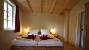 Ein Doppelbett mit weißen Bettwäsche und roten Zierkissen, ein Holz-Kopfstück, Nachttischlampen und ein Holzboden.
