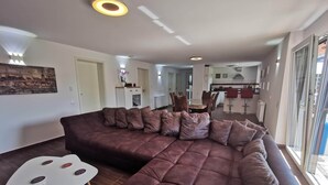 A modern living room with a large sectional sofa, a dining table, and a kitchen in the background.